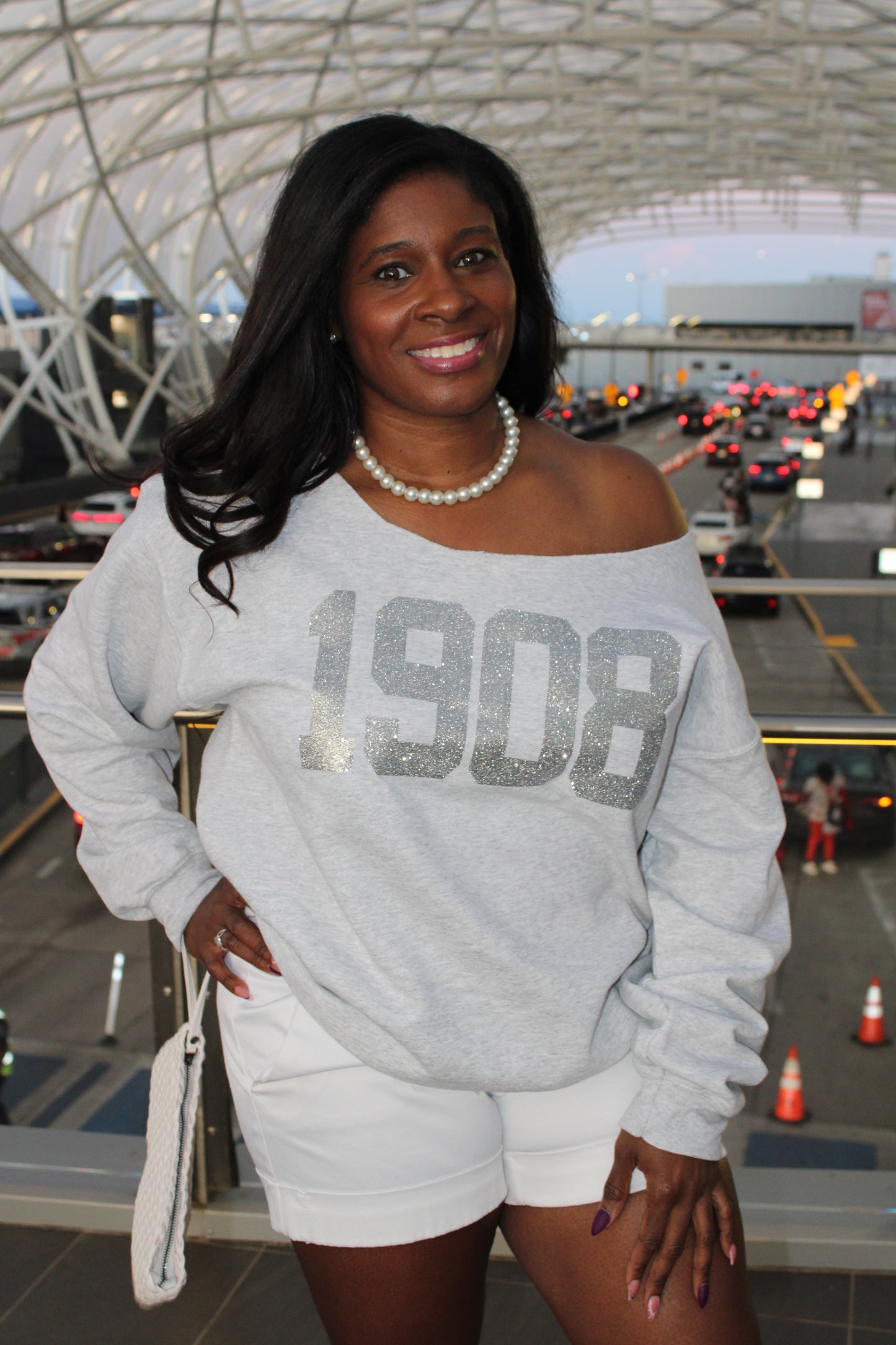 Woman wearing a gray sweatshirt with 'BOSS' text, standing in an urban setting. 1908 AKA Silver Glitter on Ash Grey Sweatshirt