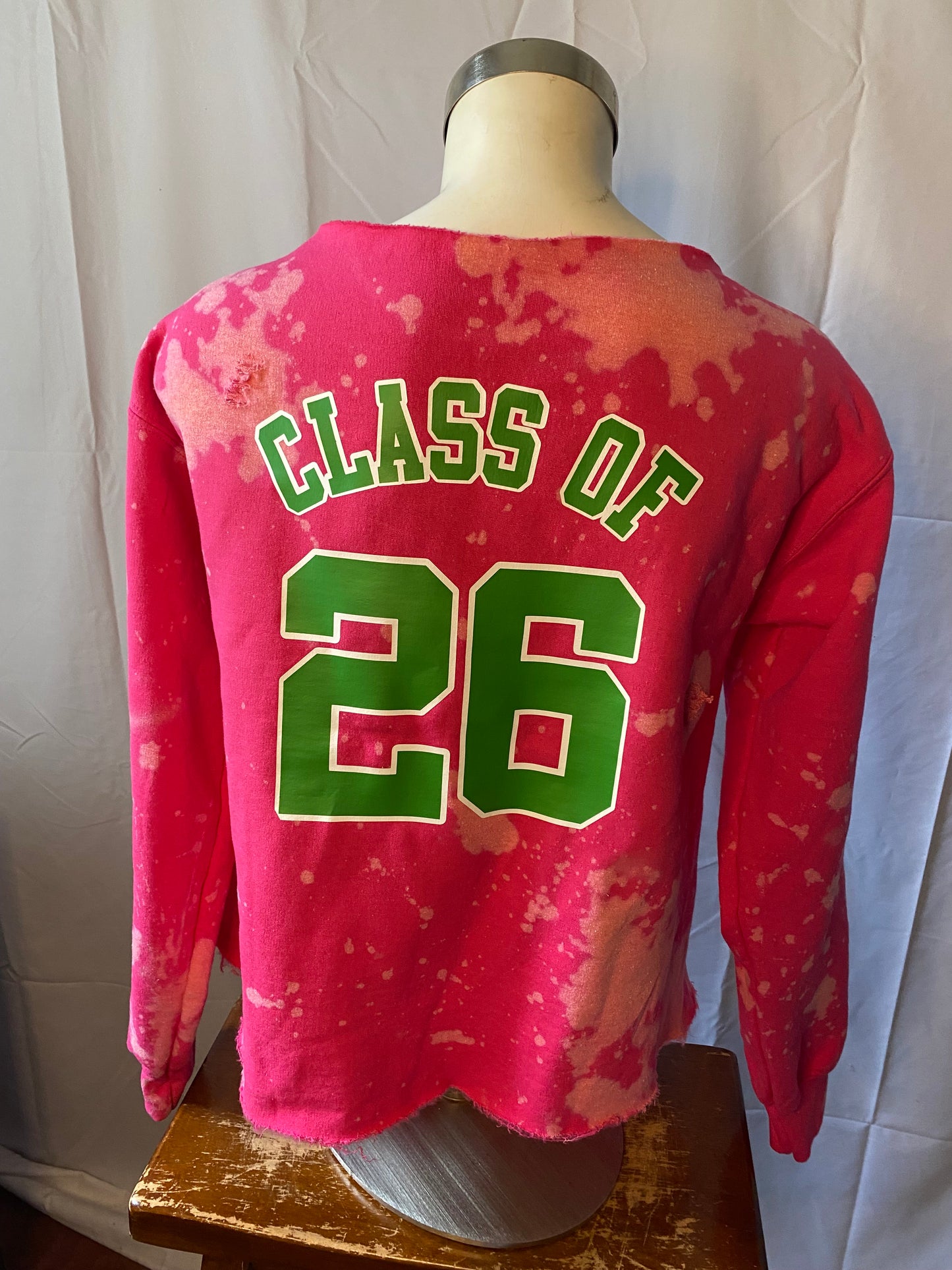 Pink sweatshirt with 'Class of 26' text on a mannequin against a white background