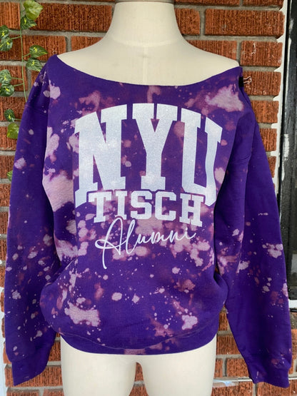 Purple sweatshirt with 'NYU Tisch Alumni' text on a mannequin against a brick wall.