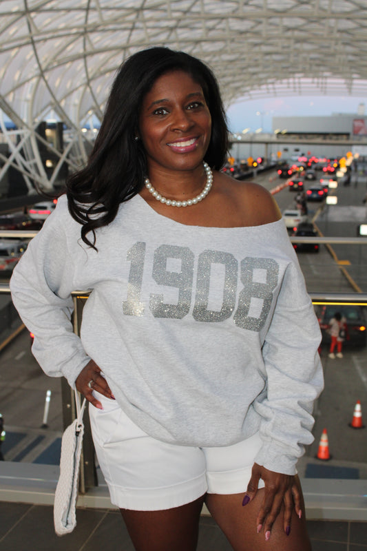 Woman wearing a gray sweatshirt with 'BOSS' text, standing in an urban setting.  1908 AKA Silver Glitter on Ash Grey Sweatshirt