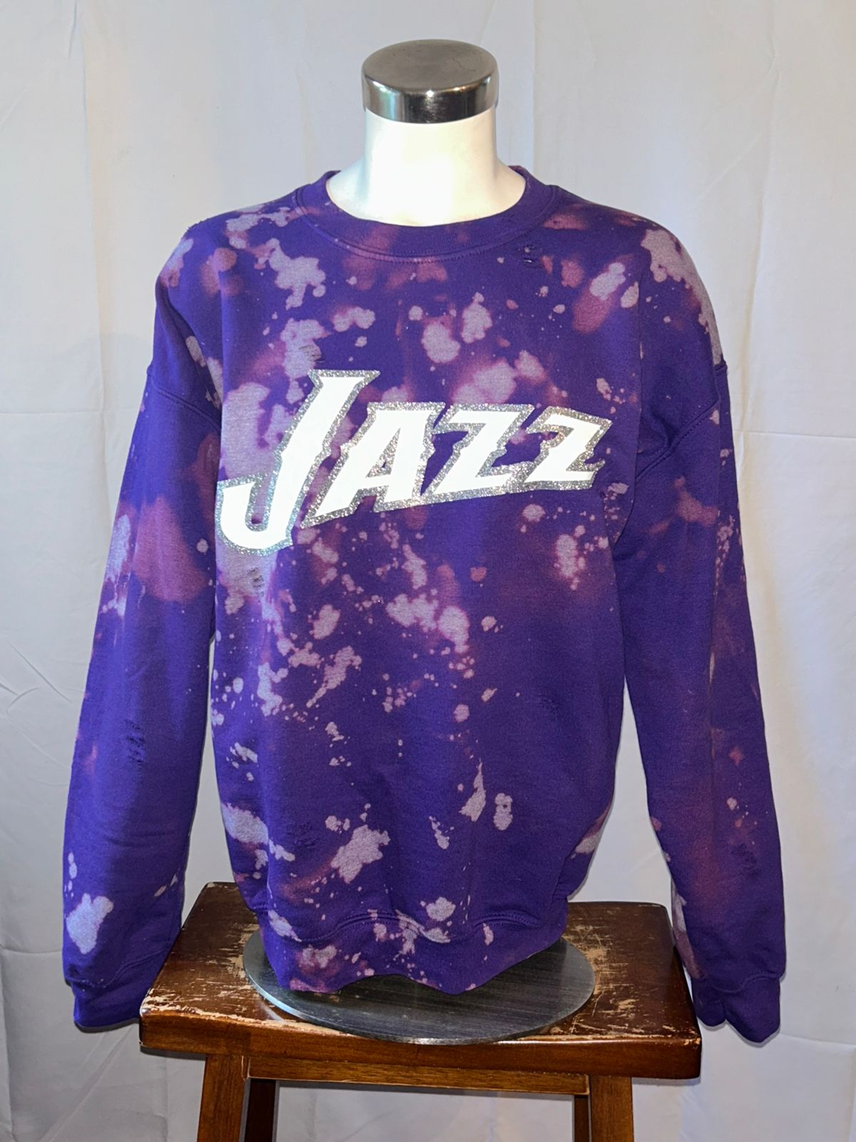 Purple tie-dye sweatshirt with 'Jazz' text on a mannequin against a white wall.